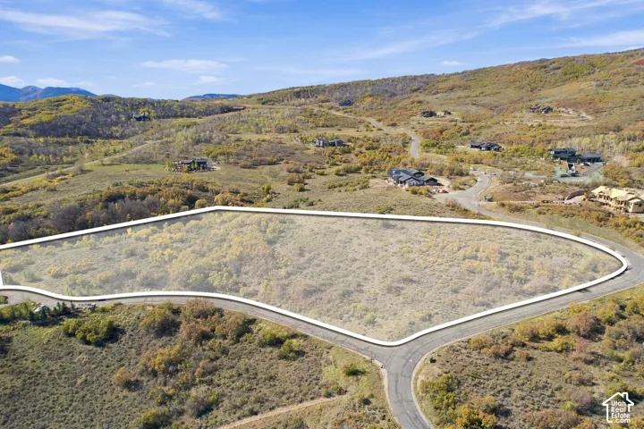 Vacant residential lot featuring paved road frontage, natural topography, and native vegetation, set against a mountainous landscape