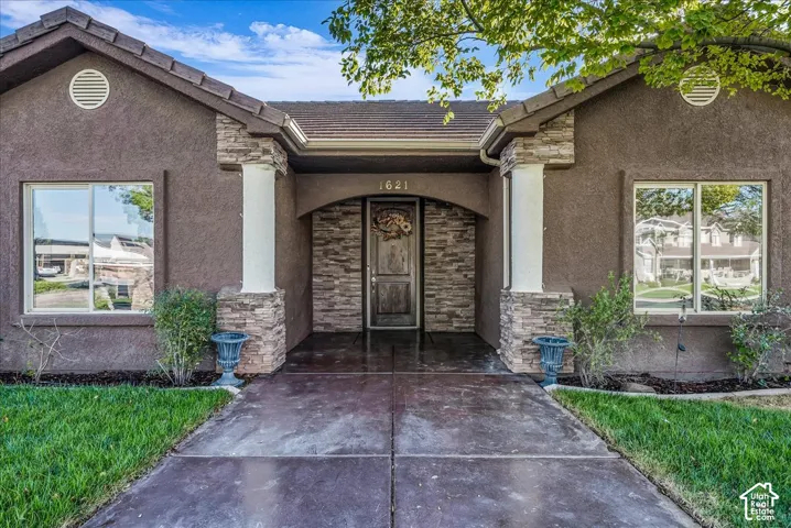 Stucco exterior featuring stacked-stone accents, arched entryway, column supports, and a stained concrete walkway
