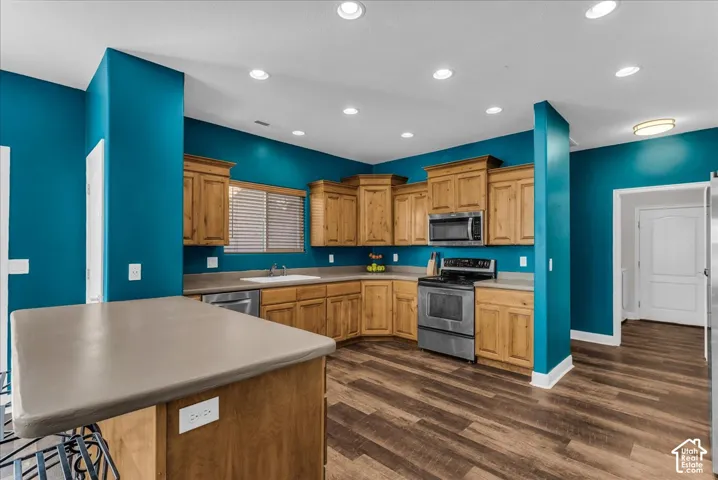 Kitchen featuring natural wood cabinetry, solid-surface countertops, wood-finish flooring, integrated stainless steel appliances, and recessed lighting