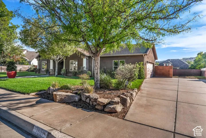 Stucco exterior featuring stone accents, a concrete driveway, a tiled roof, and a landscaped front yard with boulder rock features