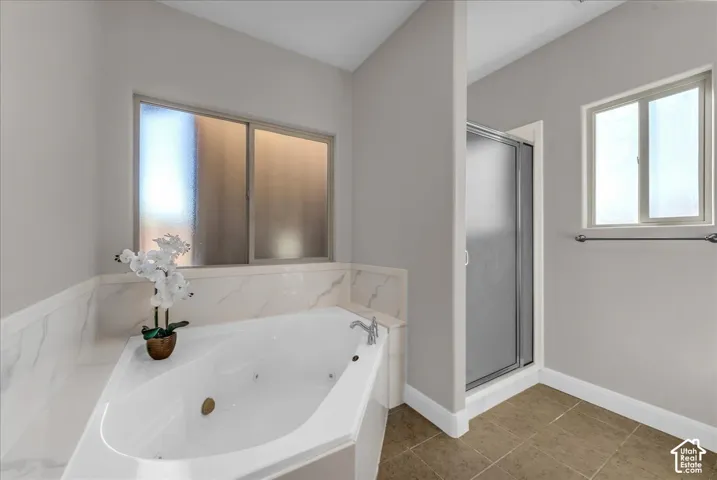 Corner jetted tub featuring stone-patterned tile surround, separate glass-enclosed shower, neutral wall tones, and tiled flooring