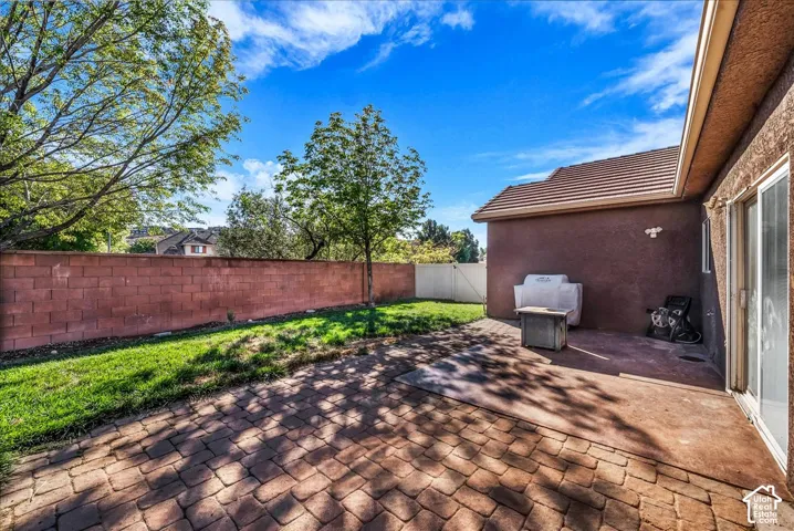 Private backyard featuring a paved stone patio, manicured lawn, mature trees, and a masonry perimeter wall