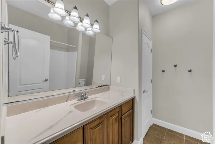 Vanity with stone-finish countertop, undermount sink, warm-toned wood cabinetry, wall-to-wall mirror, and multi-bulb vanity light fixture