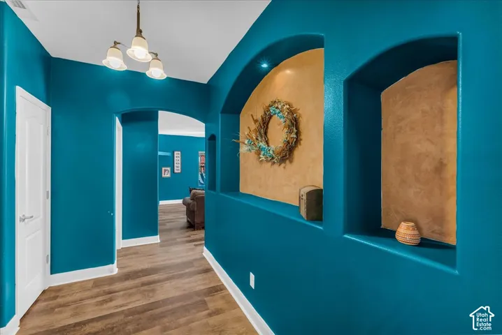 Hallway featuring arched wall niches with textured backdrops, wood-finish flooring, and a multi-light chandelier