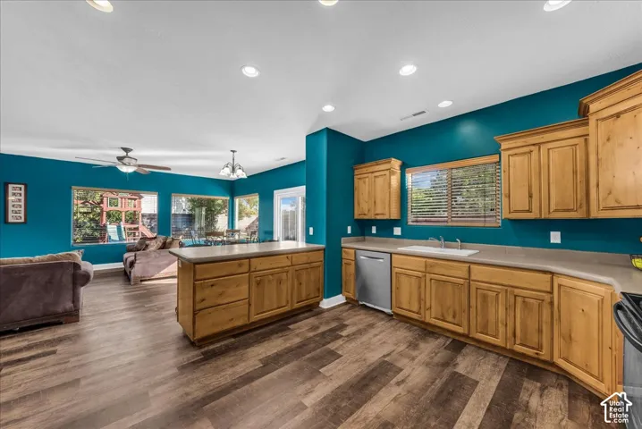 Kitchen featuring wood cabinetry, solid-surface countertops, integrated sink, stainless steel dishwasher, and wood-finish flooring