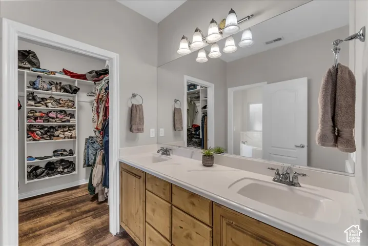 Double vanity with solid-surface countertop and undermount sinks, full-width mirror, wood-finish cabinetry, integrated shelving, and wood-finish flooring