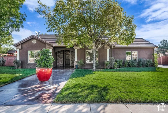 Stucco exterior featuring stone veneer accents, a tiled roof, concrete walkway, and manicured front lawn