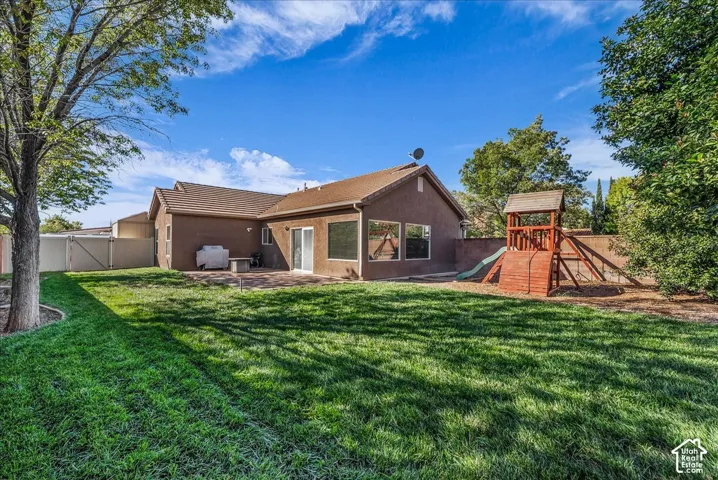 Fenced backyard featuring a manicured lawn, paved patio, mature trees, and a wooden structure