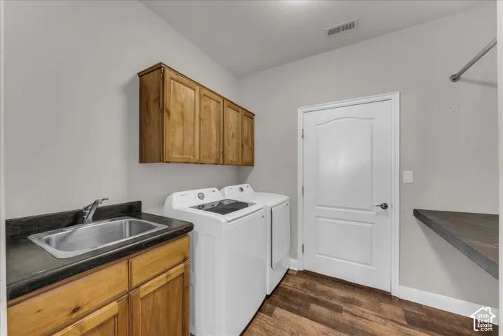 Utility room featuring wood-finish cabinetry, a drop-in stainless steel sink, dark solid-surface countertops, and wood-finish flooring