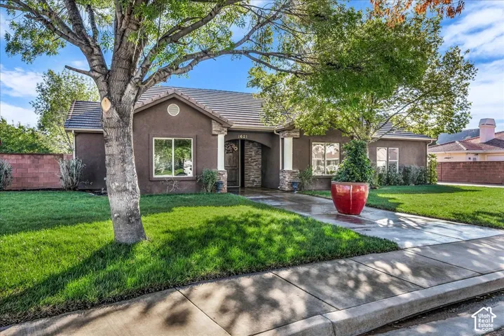 Single-story exterior featuring a stucco facade, stone-accented entryway columns, a concrete driveway, and mature landscaping