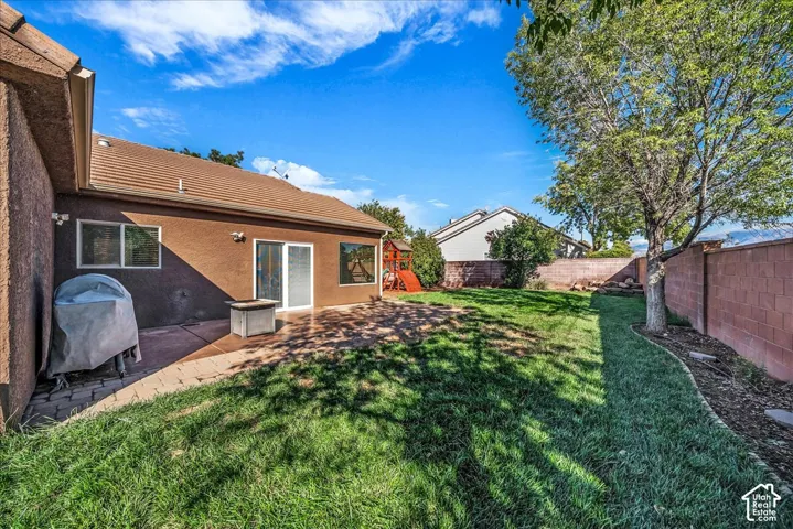 Expansive backyard featuring a concrete patio, perimeter masonry wall, mature trees, and a landscaped lawn