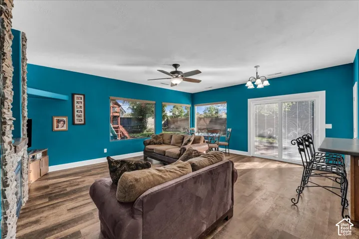 Living space featuring wood-finish flooring, stone-accented fireplace, ceiling fan, and sliding glass doors