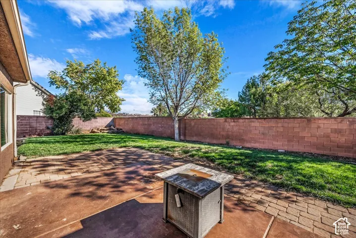 Private backyard featuring a paved concrete patio, a grass lawn, and a perimeter masonry wall with mature trees