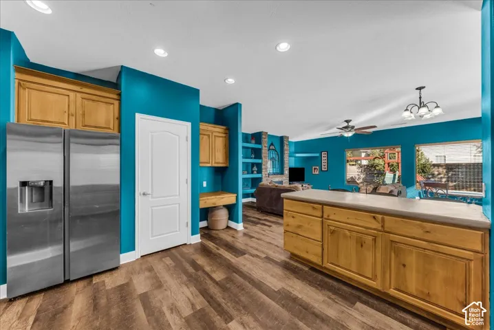 Wood-finish flooring, stainless steel refrigerator, kitchen island with solid-surface countertop, natural wood-finish cabinetry, and built-in shelving