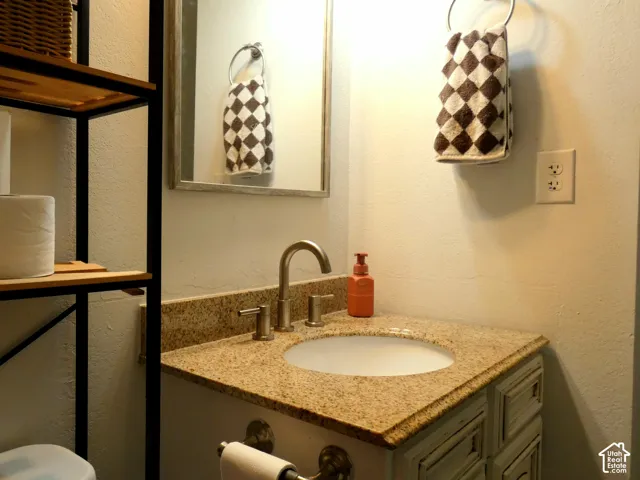 Vanity featuring a stone-composite countertop, undermount sink, brushed nickel faucet, and cabinetry with recessed-panel detailing