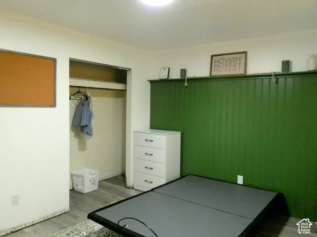 Room interior featuring a floor-to-ceiling vertical plank wall accent, wood-finish flooring, and a walk-in closet with an overhead shelf