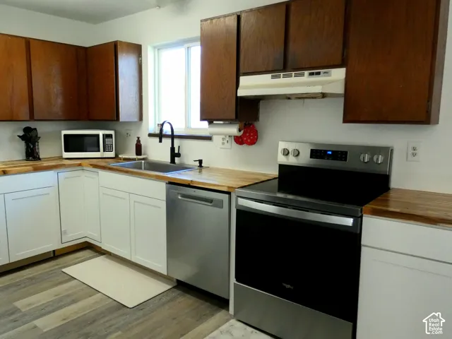 Kitchen featuring white lower cabinetry, stained-wood upper cabinetry, butcher block countertops, stainless steel appliances, and wood-finish flooring