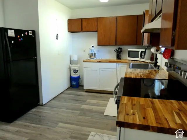 Kitchen featuring butcher-block countertops, wood-finish flooring, white lower cabinetry, dark-toned upper cabinetry, and a stainless steel range