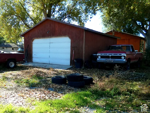 Detached wood-sided garage featuring a white overhead door and mature canopy trees