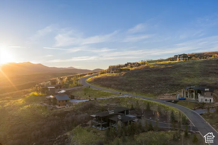 Aerial perspective of a hillside residential community featuring paved roads, custom multi-story residences, mature evergreen trees, and expansive mountain terrain