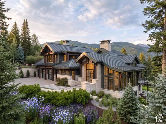 Custom stone exterior featuring a multi-gabled metal roof, expansive floor-to-ceiling windows, timber accents, and a paved stone courtyard