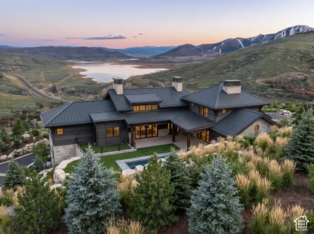 Custom residence featuring a standing-seam metal roof, stone and dark-tone siding, multiple stone chimneys, an integrated swimming pool, and tiered landscaping
