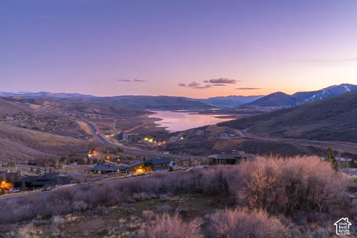 Panoramic landscape featuring mountain terrain, a large reservoir, and native vegetation under a sunset sky