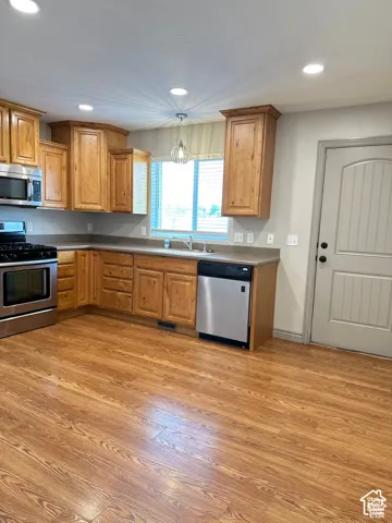 Kitchen featuring wood cabinetry, stainless steel appliances, wood-finish flooring, recessed lighting, and a neutral countertop