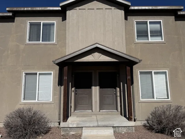 Two-story exterior featuring a neutral stucco finish, vertical board-and-batten siding accents, a covered entryway with decorative support beams, and double entry doors