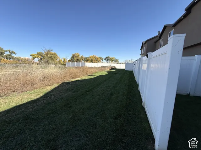 Private backyard featuring a manicured lawn and a full-height white vinyl privacy fence