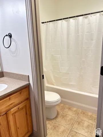 Bathroom featuring a wood-finish vanity with a stone-composite countertop, integrated sink, matte black circular towel ring, ceramic tile flooring, and a tub-shower combination
