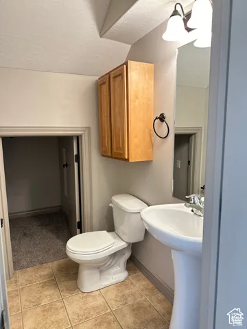 Bathroom featuring a white pedestal sink, dual-handle faucet, wall-mounted wood-finish cabinetry, ceramic tile flooring, and a flush-mount light fixture
