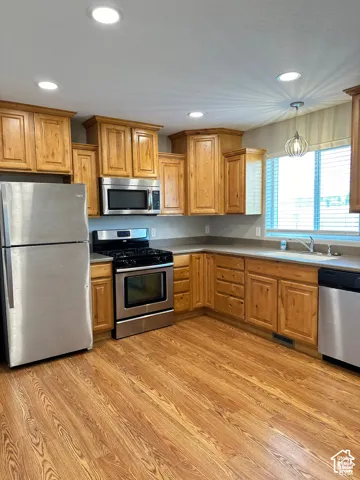 Kitchen featuring wood cabinetry, stainless steel appliances, recessed lighting, a pendant light fixture, and wood-finish flooring