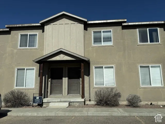 Two-story exterior featuring stucco siding, gabled roofline, dark-toned wooden support posts, and concrete steps