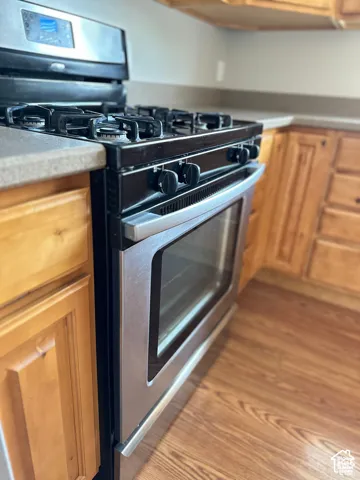 Stainless steel gas range with a digital control panel, wood-finish cabinetry, and wood-finish flooring
