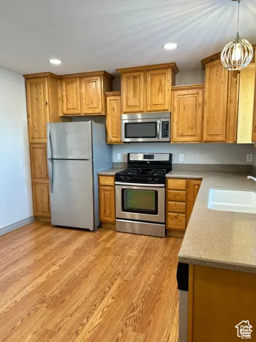 Kitchen featuring wood cabinetry, stainless steel appliances, solid-surface countertops, wood-finish flooring, and recessed lighting
