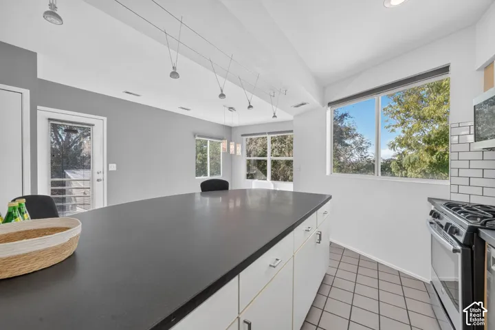 Kitchen featuring a large central island with solid-surface countertop, white cabinetry, tile flooring, subway tile backsplash, and cable-mounted track lighting