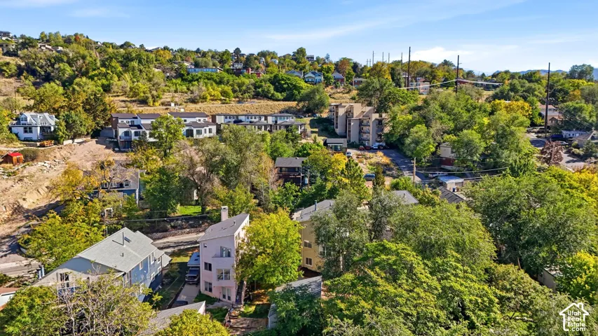 Aerial perspective featuring a multi-level residential structure with a sloped roofline, set within a hillside landscape characterized by mature trees and varied foliage