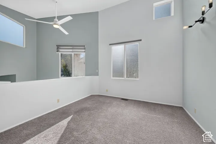 Vaulted ceilings featuring multi-level windows, wall-mounted multi-bulb lighting, and a neutral-toned ceiling fan