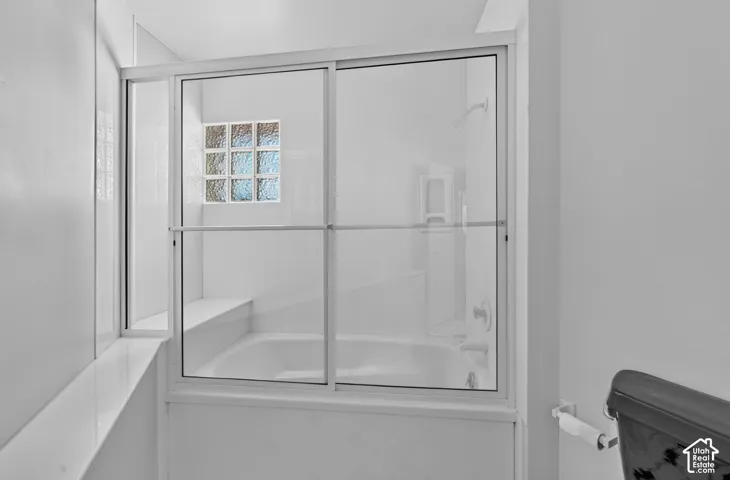 Bathtub and shower combination featuring a glass slider enclosure, built-in tub deck, and textured glass block window