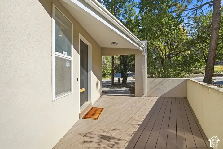 Covered exterior porch featuring wood-finish decking, stucco siding, and a flush-mount ceiling light