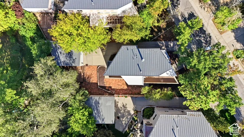 Aerial perspective of property featuring a metal roof, concrete driveway, stone hardscaping, and mature trees