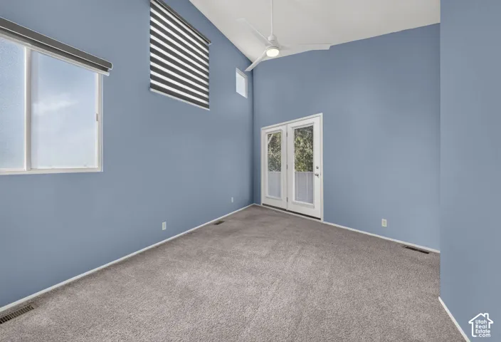 Vaulted ceiling featuring a ceiling fan, multiple windows with neutral-toned treatments, and glass-paneled double doors