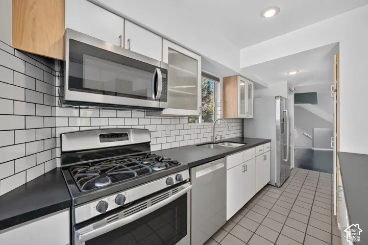 Kitchen featuring white flat-panel cabinetry, dark solid-surface countertops, subway tile backsplash, stainless steel appliances, and ceramic tile flooring