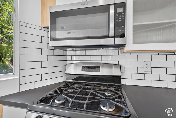 Stainless steel gas range with overhead microwave, white subway tile backsplash, and dark solid-surface countertops