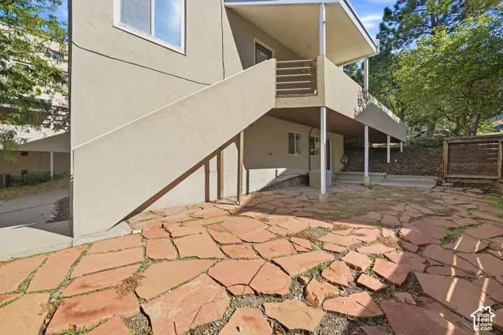 Stucco exterior featuring a raised balcony with metal railings, a stone-paved patio, and a covered ground-level area