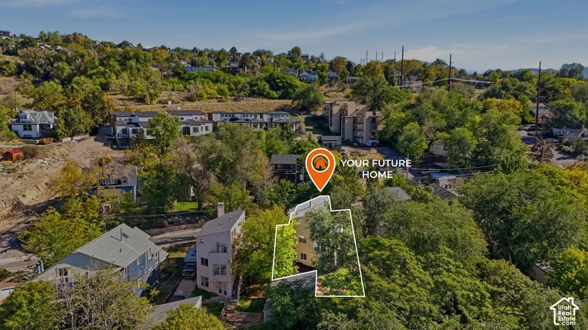 Aerial perspective of a multi-story residential structure featuring a light-toned exterior, a pitched roofline, and significant mature tree coverage on a sloped lot