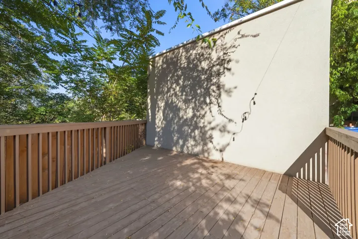 Outdoor deck featuring wood plank flooring and vertical wood balustrade railings against a stucco exterior wall