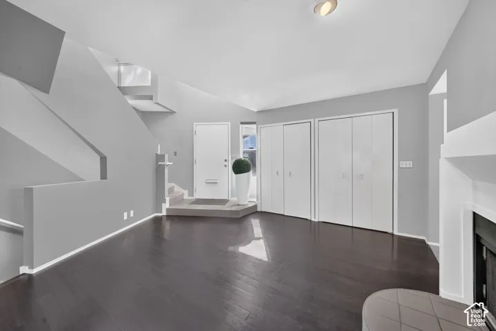 Open-concept room featuring dark wood-finish flooring, a neutral color palette, dual floor-to-ceiling closets with white panel doors, and a tiled entry landing