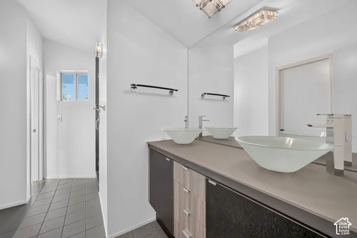 Dual vessel sinks, solid-surface countertop, mixed-material floating vanity, full-width wall mirror, and large-format tile flooring